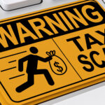 Yellow warning sign on keyboard key, depicting tax scam alert with running figure and money bag, symbolizing online financial fraud prevention